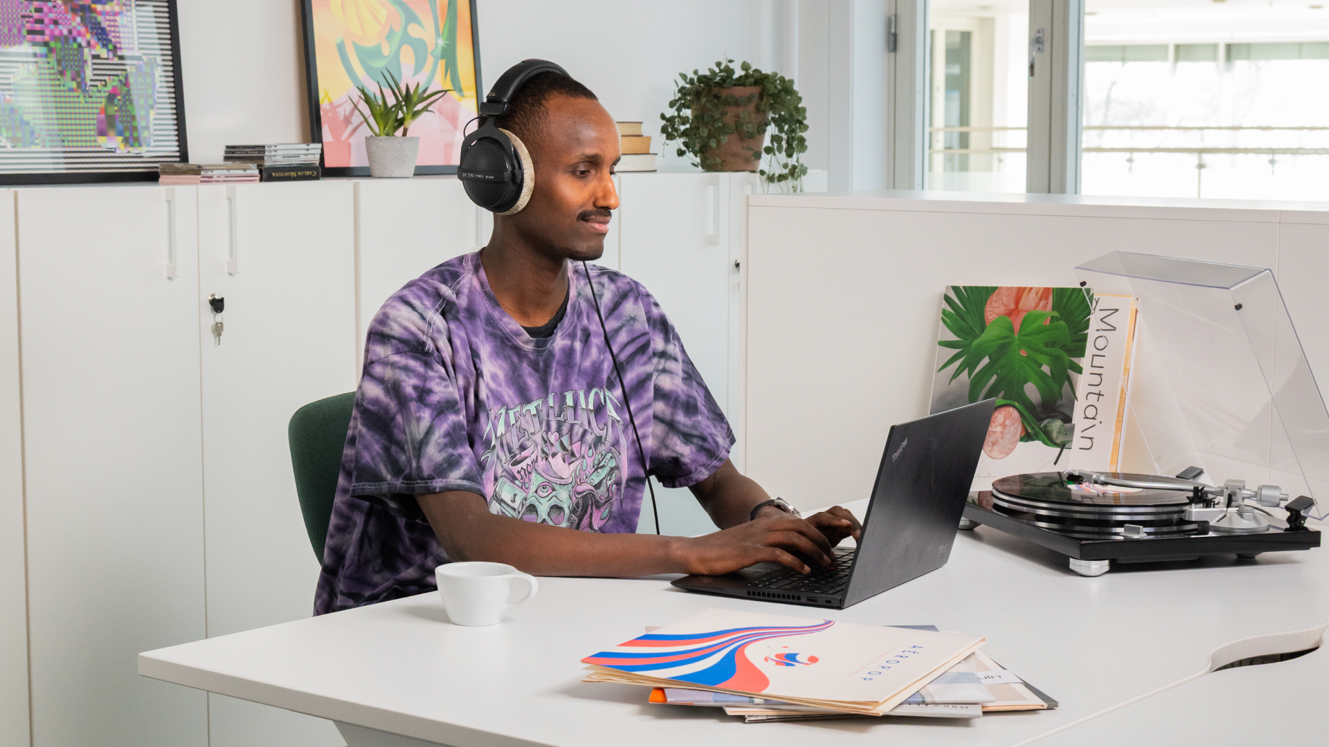 En mann sitter i et kontorlandskap foran en PC . Ved siden av ham står en platespiller